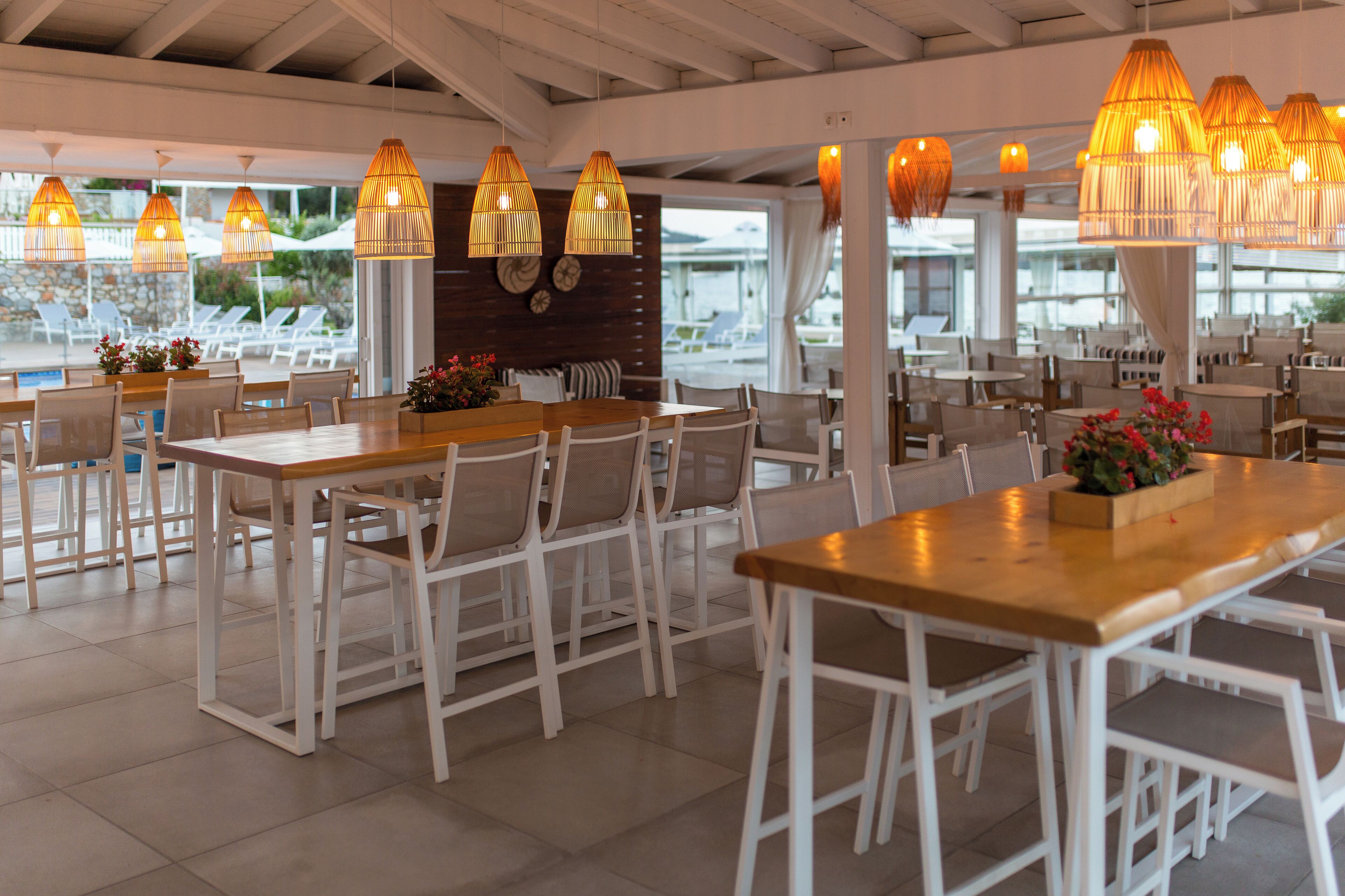 A restaurant with white furniture, large windows, and hanging lamps.