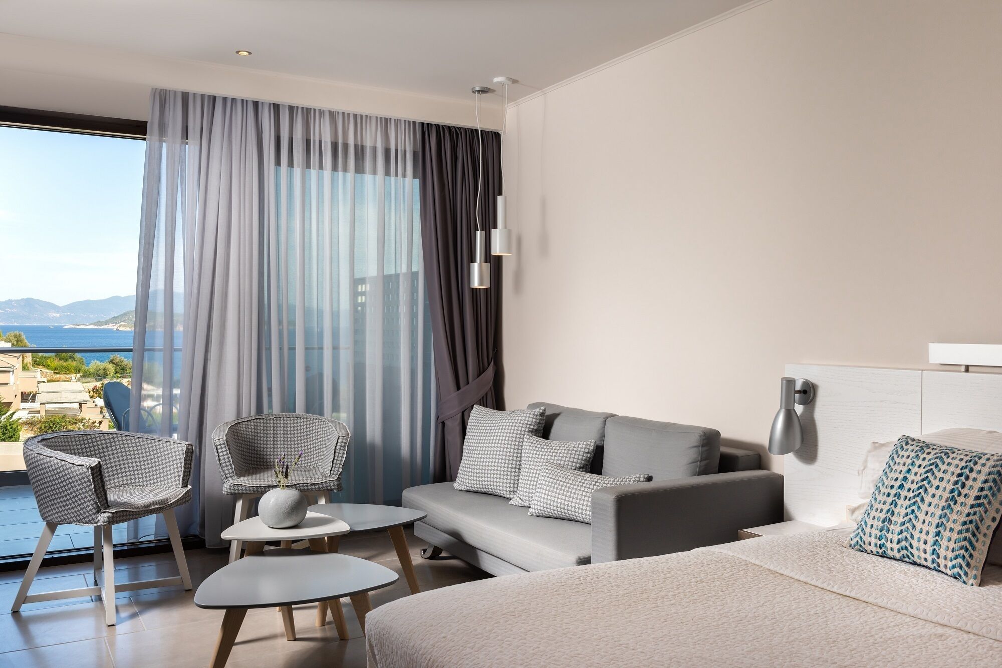 A modern hotel room with a balcony, a sofa, a chair, and a small table.