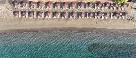 Vista aérea de una playa con filas de tumbonas y sombrillas, agua turquesa cristalina y una orilla arenosa.