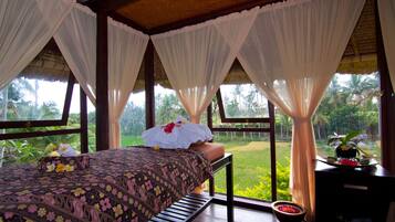 Relax in a serene room with a view of lush green surroundings, featuring a comfortable bed and a charming table with a bowl of fresh fruit and a potted plant.