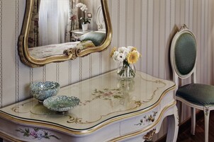 Un tocador de estilo vintage con detalles ornamentales, un espejo y un jarrón con flores.
