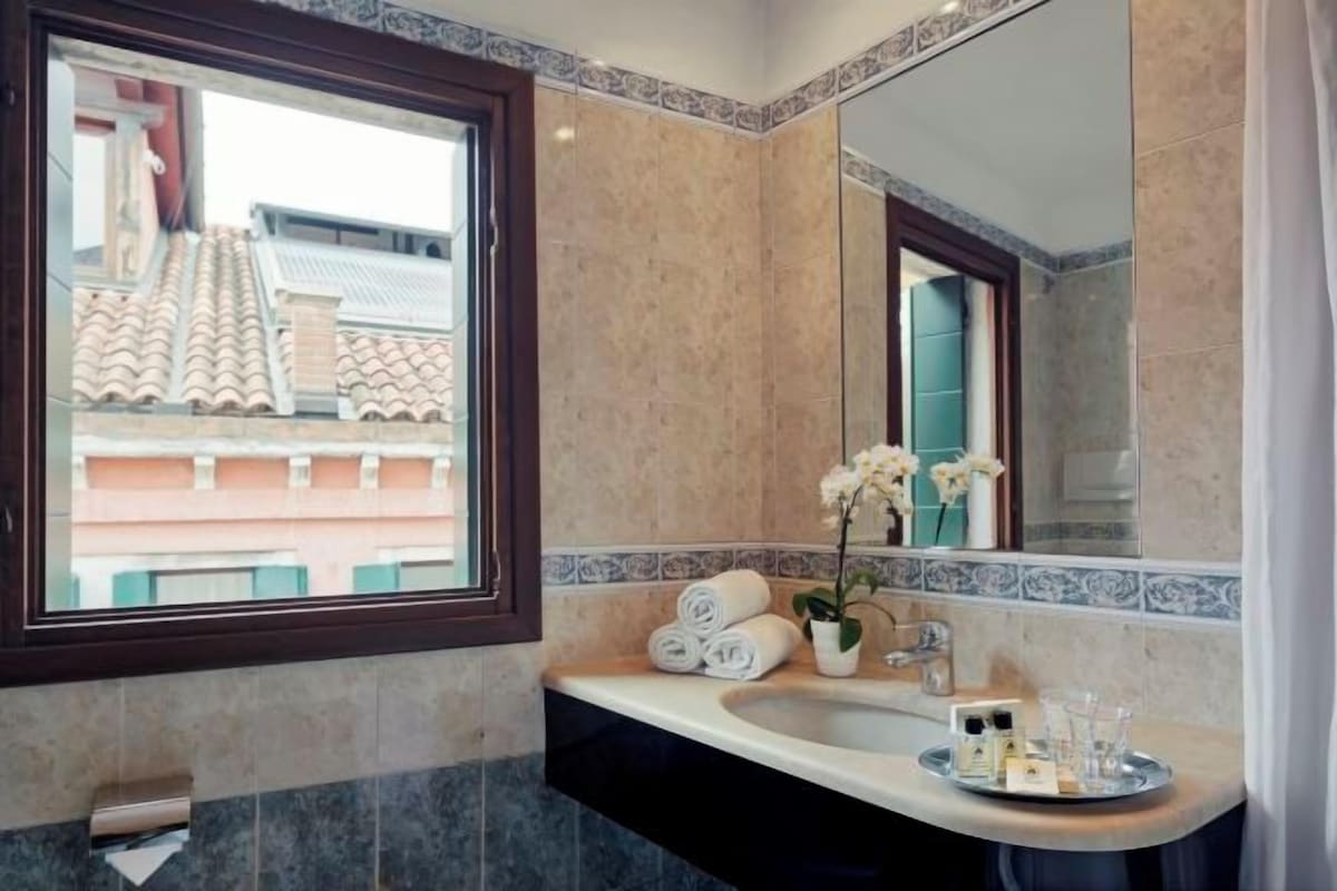 A bathroom with a large window, a sink with toiletries, and a mirror.