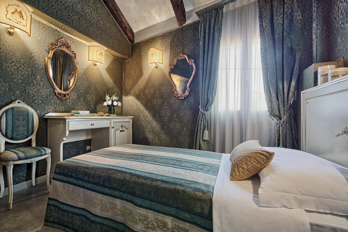 Een slaapkamer met een groot bed, een bureau, een stoel en twee spiegels aan de muur.