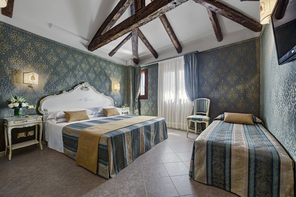 Een slaapkamer met een groot bed, een kleiner bed, een nachtkastje en een stoel.