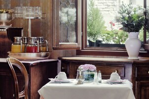A dining table set with white tableware, a vase with flowers, and a window view of greenery.
