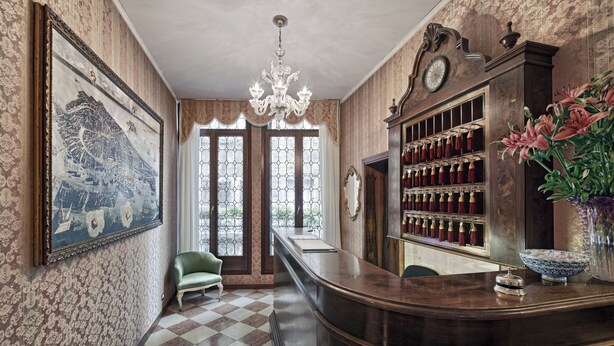 A bar area with a checkered floor, a green chair, a chandelier, a clock, and a wine rack. - Hotel Antica Locanda Al Gambero (Venice)