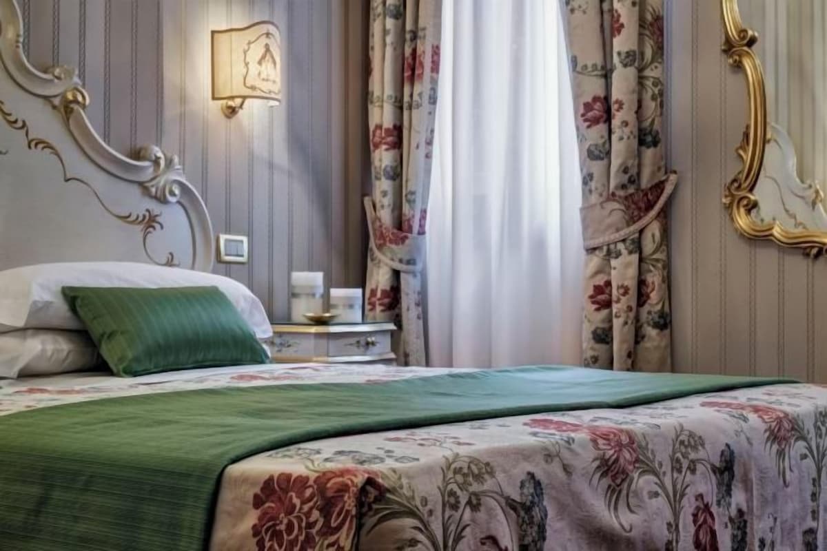 A bedroom with a bed, a nightstand, a lamp, and curtains.