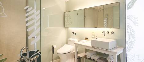 A modern bathroom with a glass shower enclosure, a white toilet, a sink with a mirror above, and a bathtub.