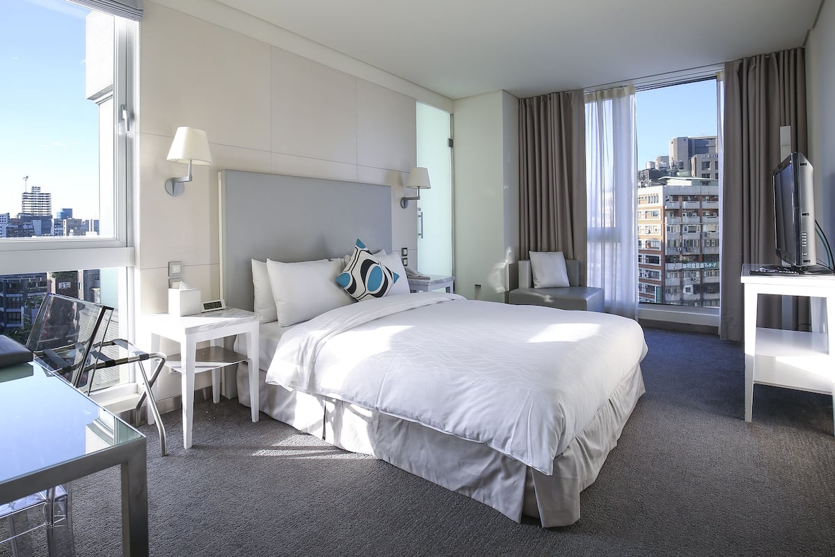Een hotelkamer met een groot bed, een bureau, een stoel, een televisie en uitzicht op de stad.