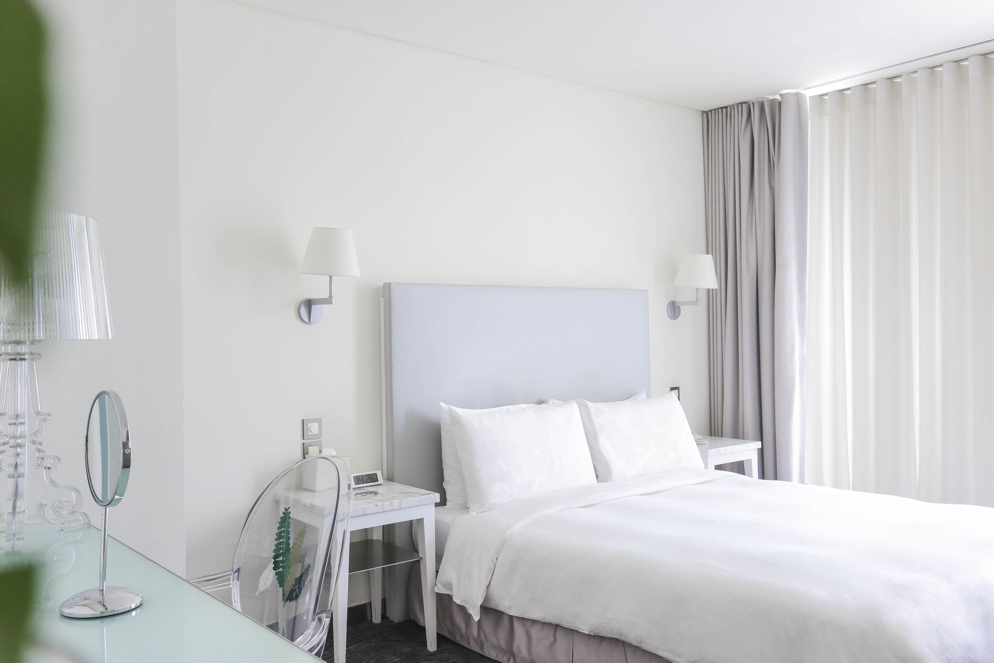 A hotel room with a bed, a desk with a lamp, a mirror, and a nightstand.