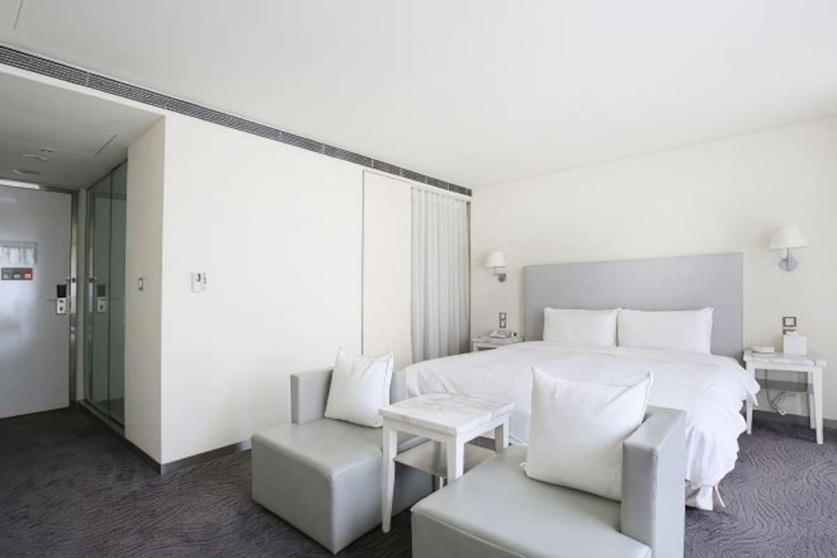 A hotel room with a bed, two armchairs, a small table, a nightstand, and a door leading to another room.