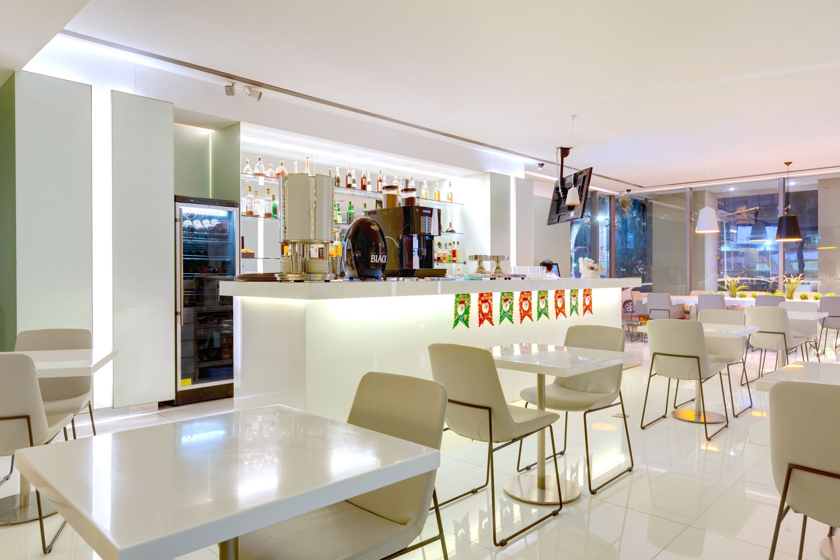 Ein modernes Restaurant mit Barbereich, weißen Tischen und Stühlen sowie einer Präsentation von Flaschen und Gläsern.