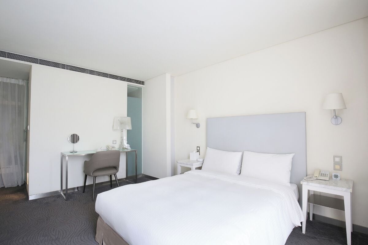 Et hotelværelse med en stor seng, et skrivebord, en stol og to sengeborde med lamper.