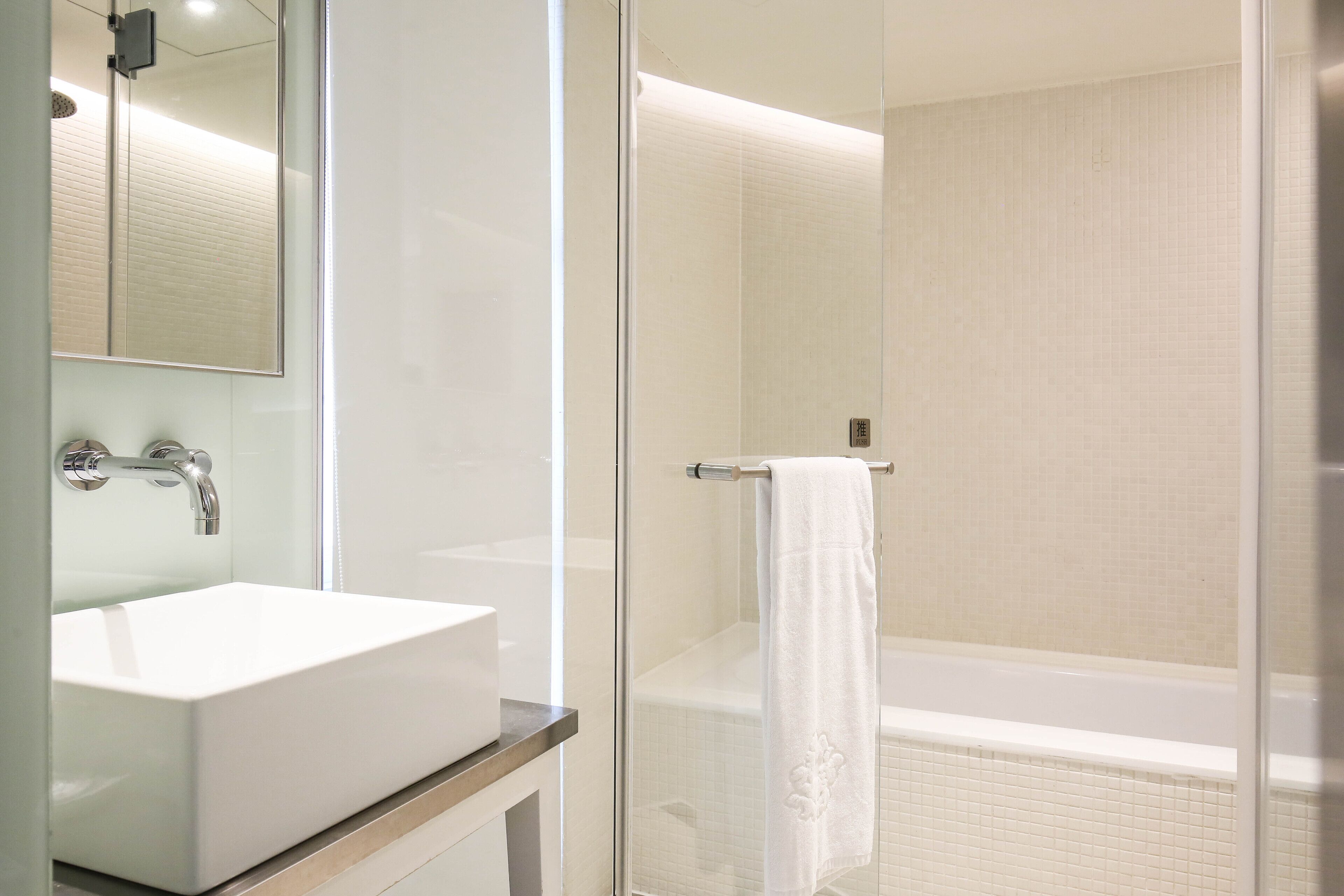 A modern bathroom with a glass shower enclosure, a white sink, and a towel hanging on the shower door.