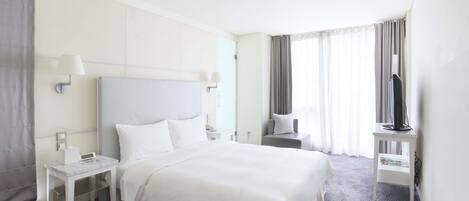 A hotel room with a large bed, a bedside table, a TV on a stand, and a window with curtains.