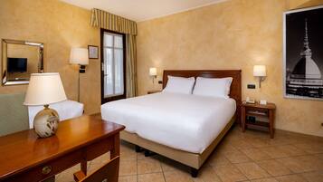 Habitación de hotel con una cama grande, dos mesitas de noche con lámparas, un escritorio con lámpara, una silla, un espejo y un cuadro en la pared.