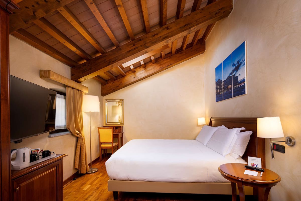 Une chambre d’hôtel avec un grand lit, un bureau avec une chaise, une télévision et une lampe fixée au mur.