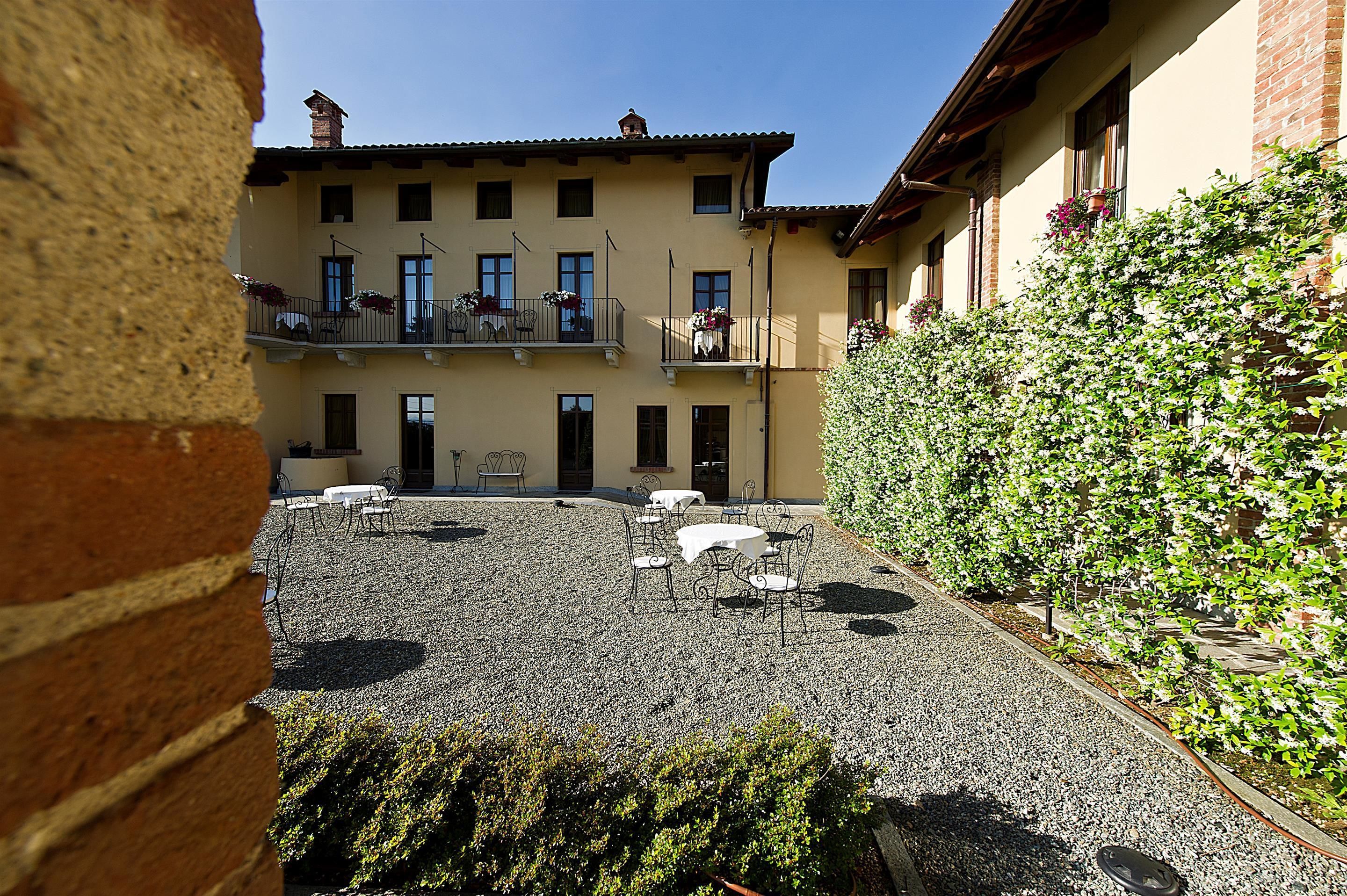 A courtyard with a building featuring a balcony, outdoor seating, and a gravel ground.