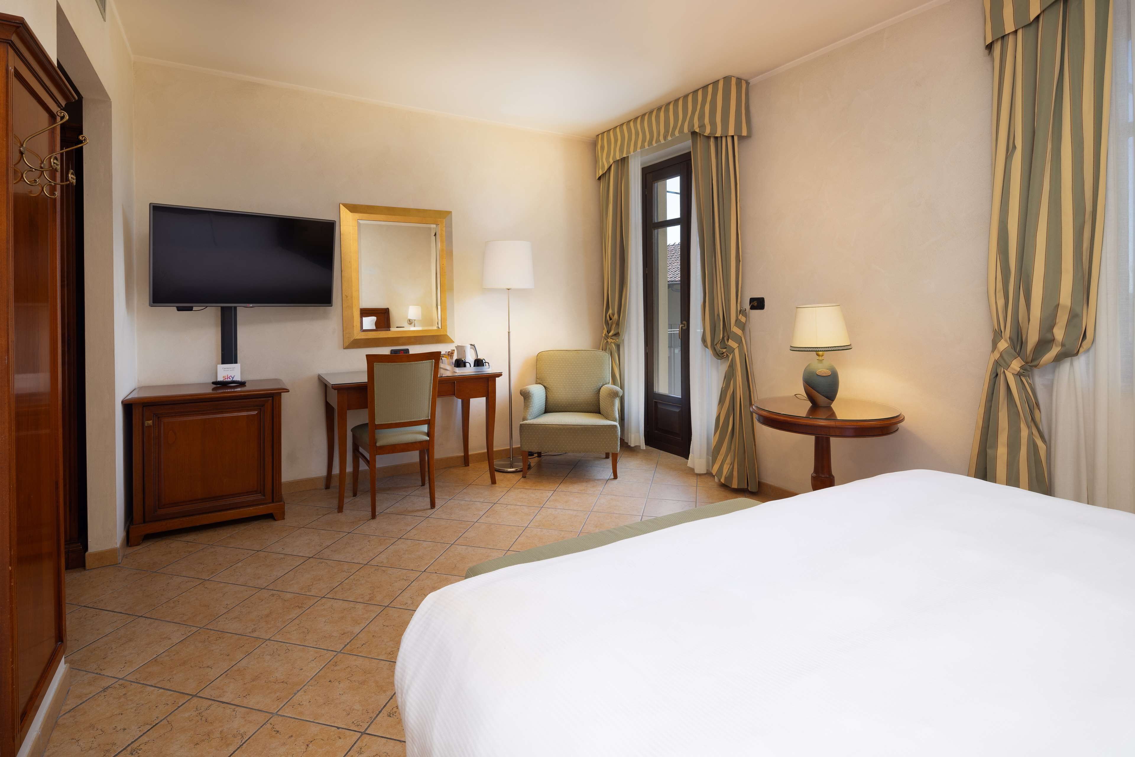 Habitación de hotel con cama, escritorio, silla, televisión, lámpara y cortinas.