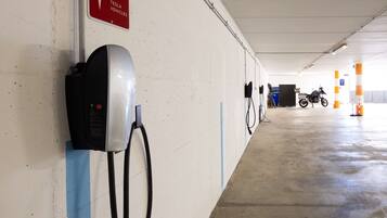 A parking garage with a Tesla charging station, a motorcycle, and orange and white pillars.