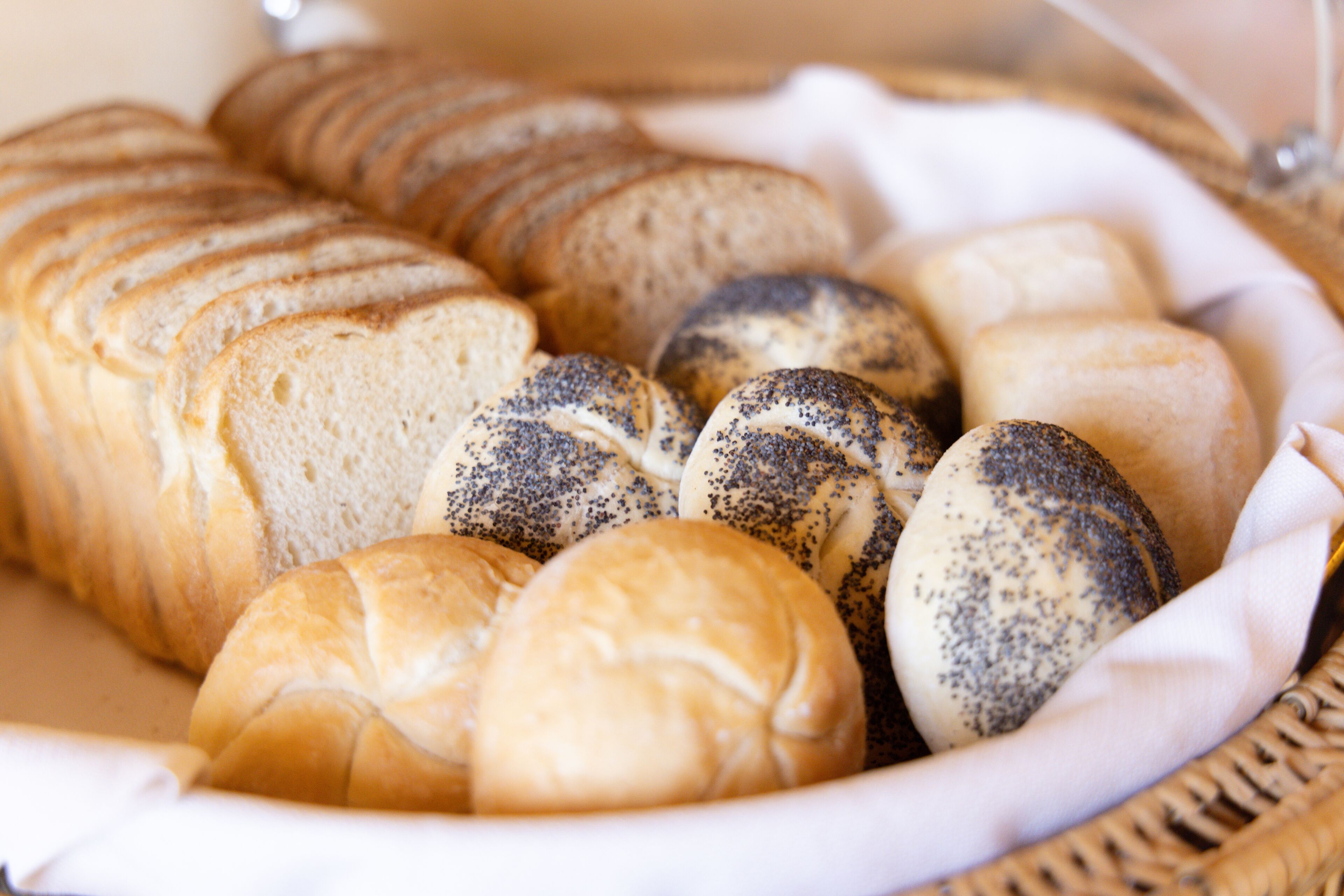 Una cesta con diferentes tipos de pan, incluyendo bollos y panes de semillas de amapola.