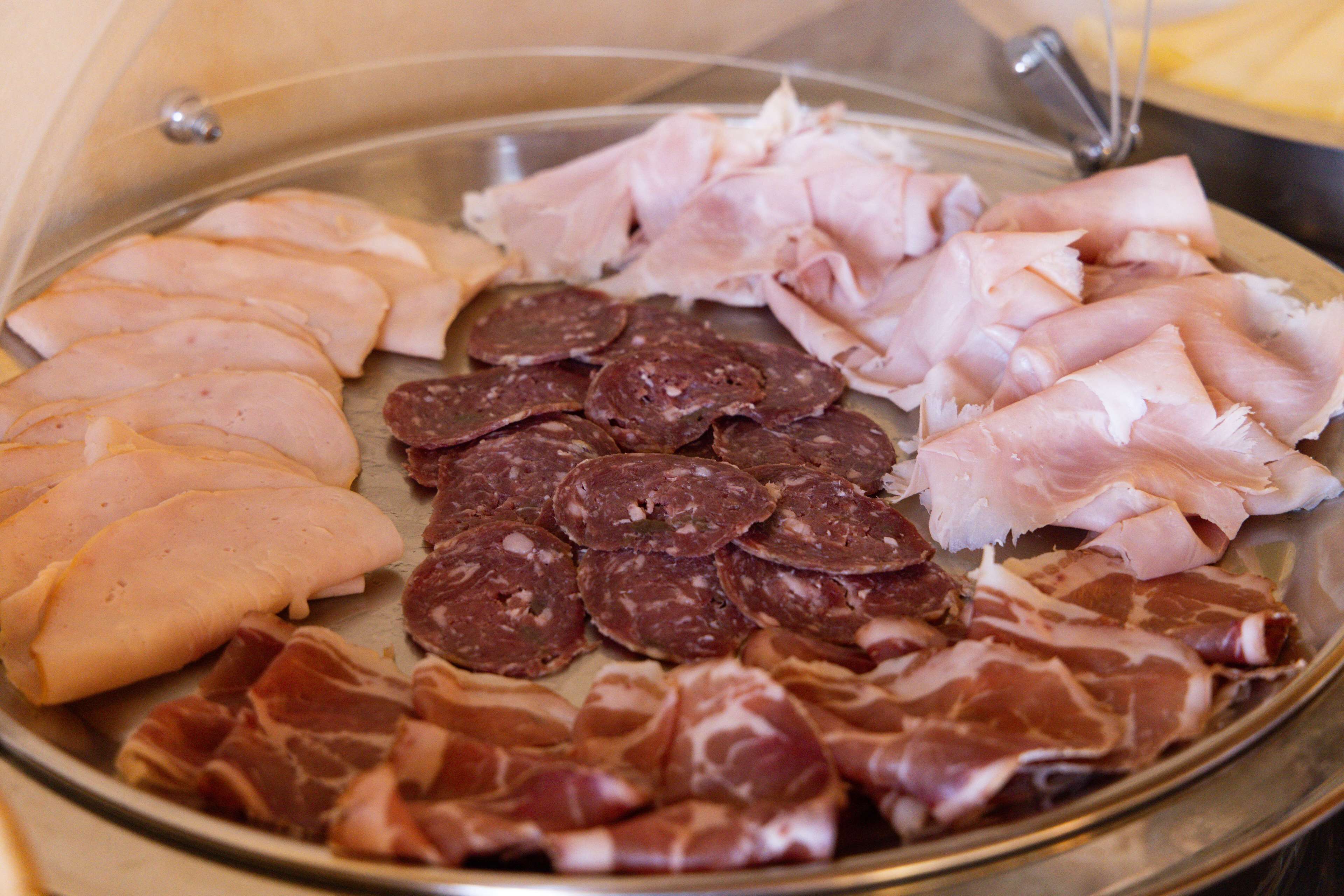 Een schotel met verschillende vleessoorten, waaronder plakjes ham, salami en parmaham.