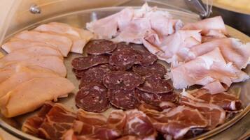 Een schotel met verschillende vleessoorten, waaronder plakjes ham, salami en parmaham.