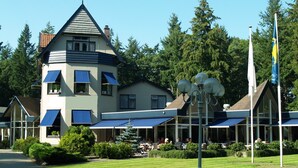 A multi-story building with a prominent tower, large windows, and a covered outdoor seating area. - Veluwe Hotel Stakenberg (Elspeet)