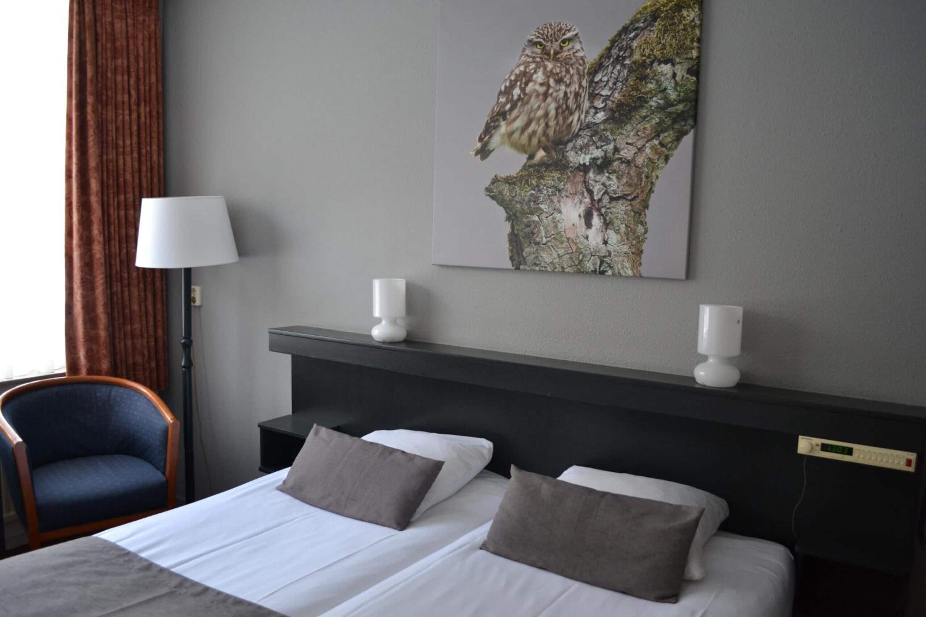 Una camera d'albergo con un letto, due comodini, una lampada, una sedia e un quadro appeso al muro.