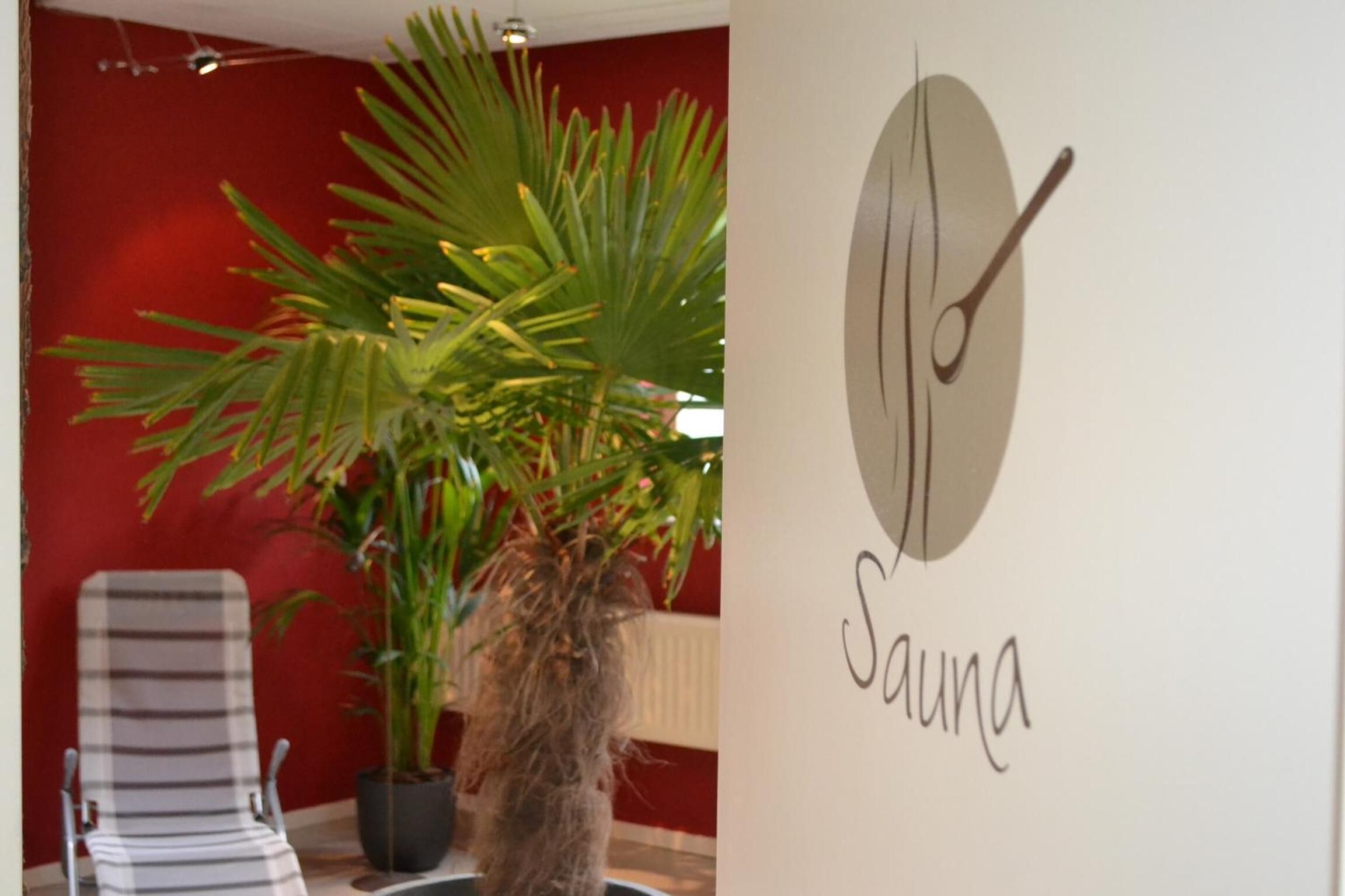 Une pièce avec une chaise à rayures, une plante en pot et un mur sur lequel est écrit le mot « Sauna ».