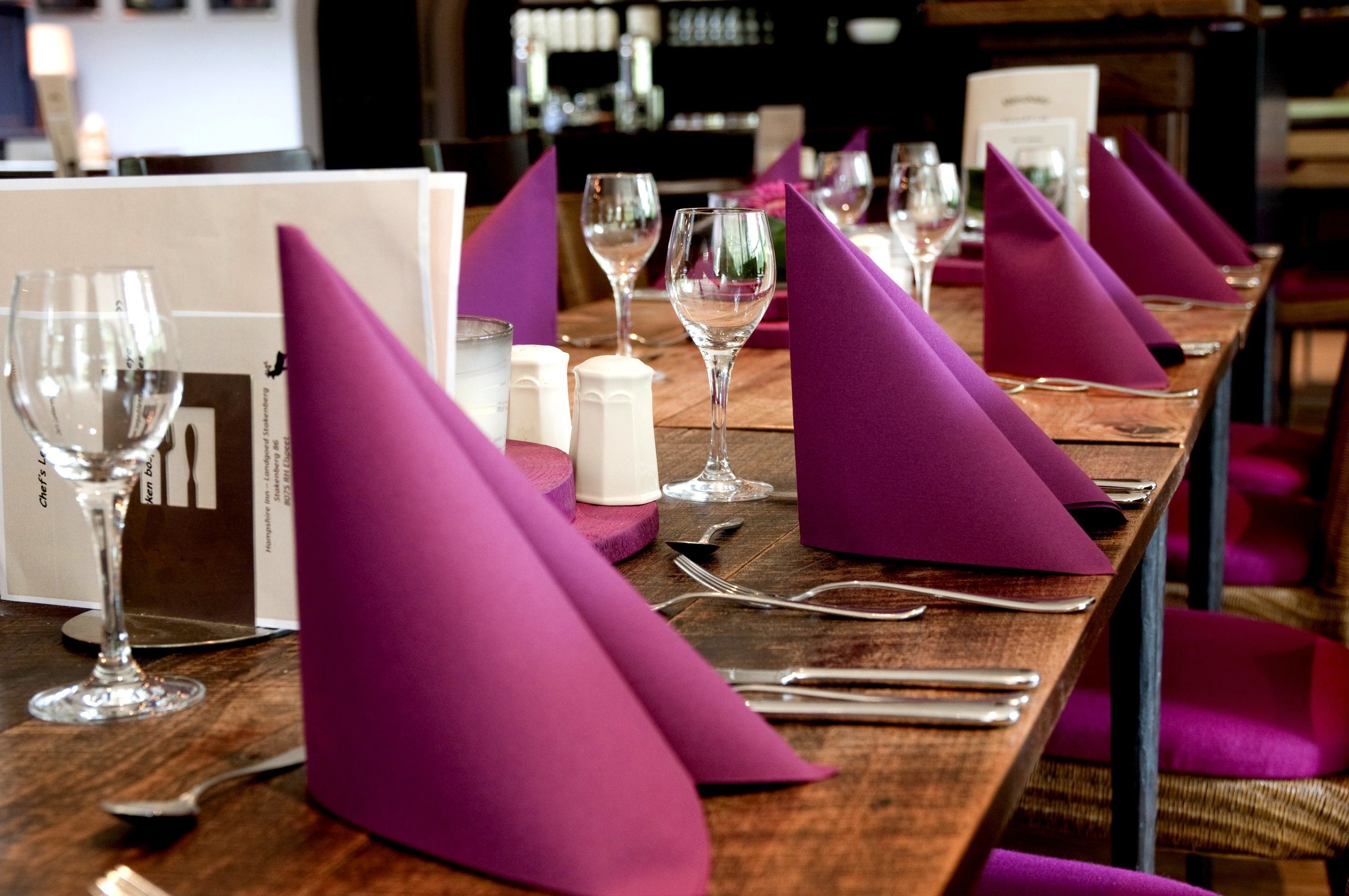 A dining table set with purple napkins, wine glasses, and cutlery.