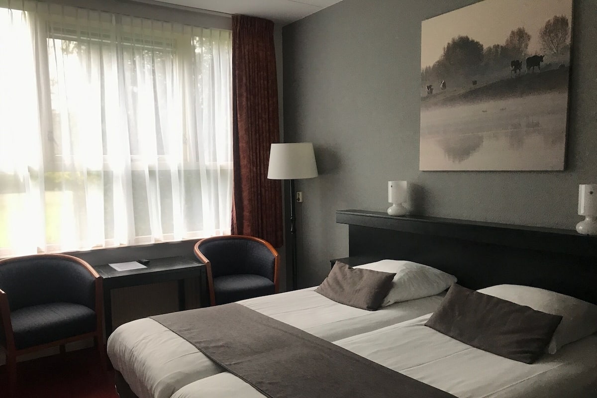 A hotel room with a large bed, two bedside tables, a desk, a chair, a lamp, and a painting on the wall.
