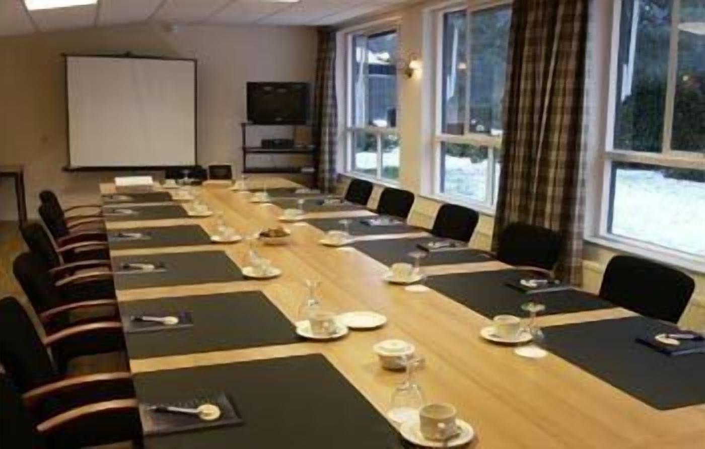 A conference room with a long table set for a meeting, equipped with chairs, a projector screen, and a television.