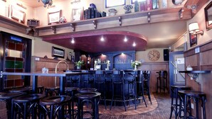 A bar area with multiple stools and a counter, wooden shelves with books and decorative items, and a clock on the wall. - Veluwe Hotel Stakenberg (Elspeet)