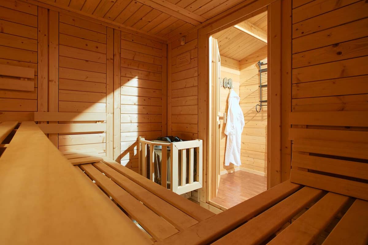 A wooden cabin with a bench, a small table, and a door leading to a room with a shower.