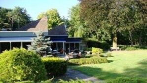 A building with a covered outdoor area, surrounded by well-maintained greenery and a lawn. - Veluwe Hotel Stakenberg (Elspeet)