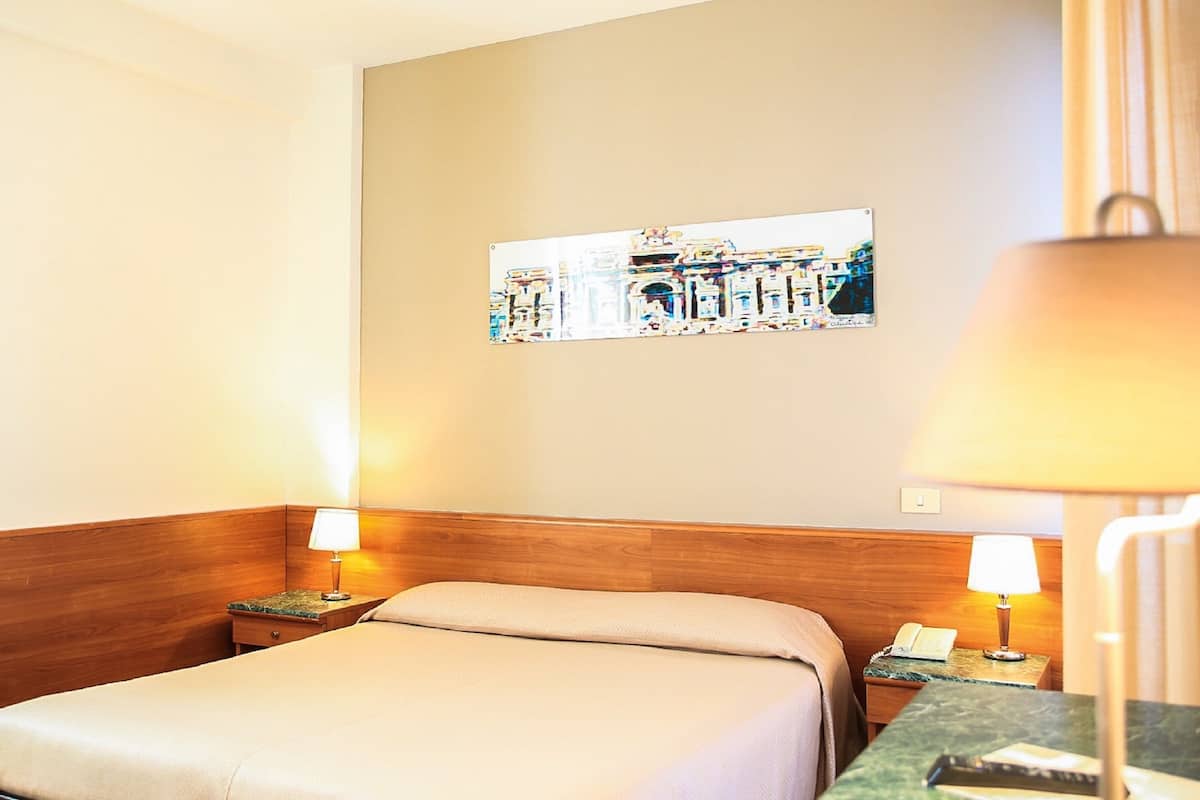 A hotel room with a bed, two bedside tables, a lamp, a picture on the wall, and a telephone.