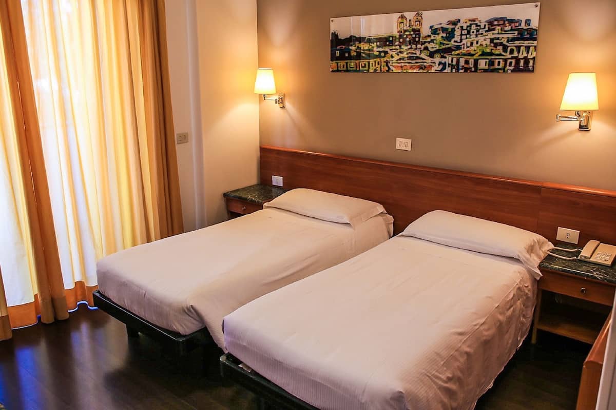 A hotel room with two single beds, a nightstand with a telephone, and a painting on the wall.
