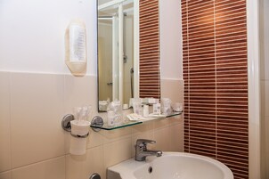 A bathroom with a glass shelf holding toiletries, a sink, and a mirror.