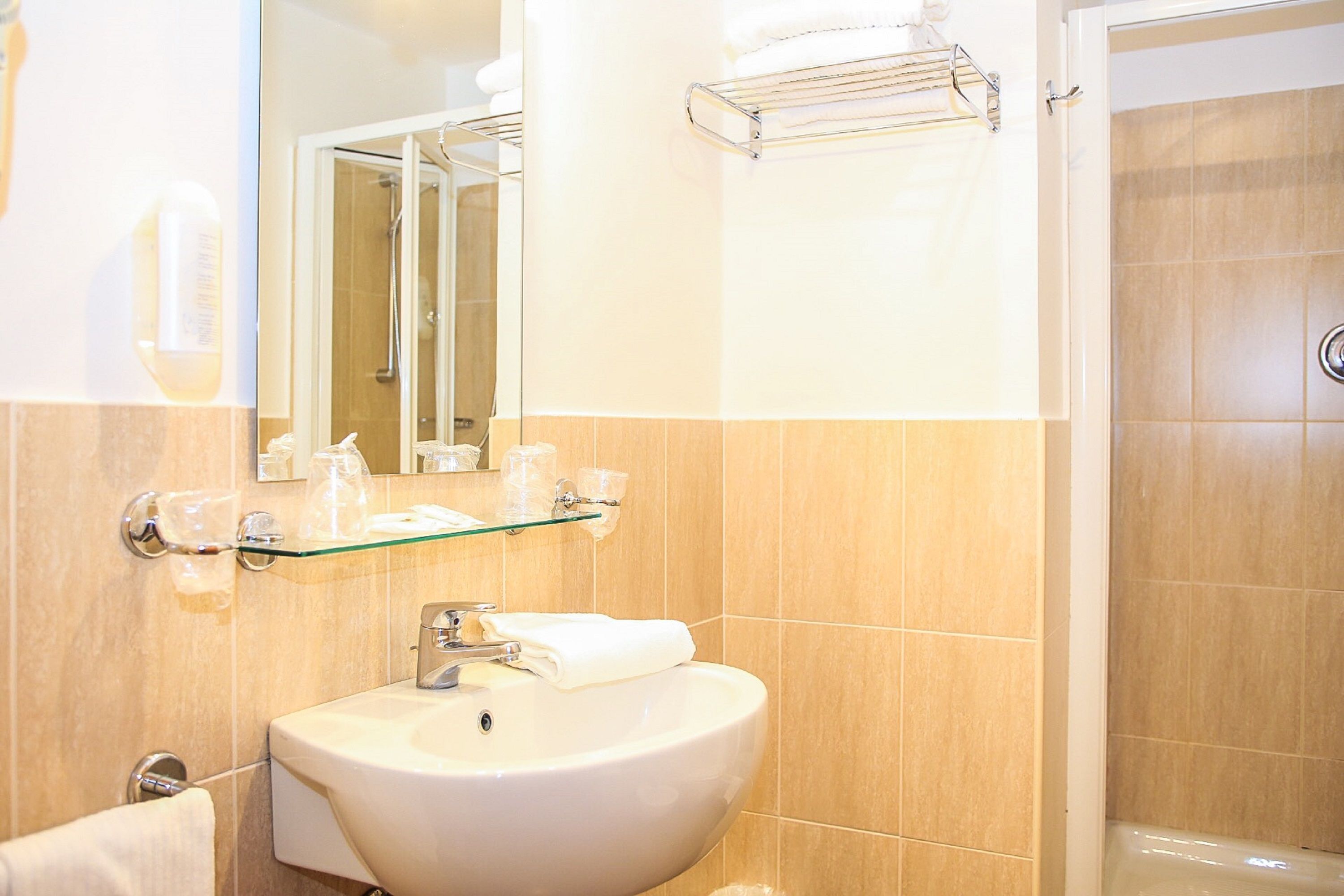 A bathroom with a white sink, glass shelf with toiletries, a mirror, and a shower area.
