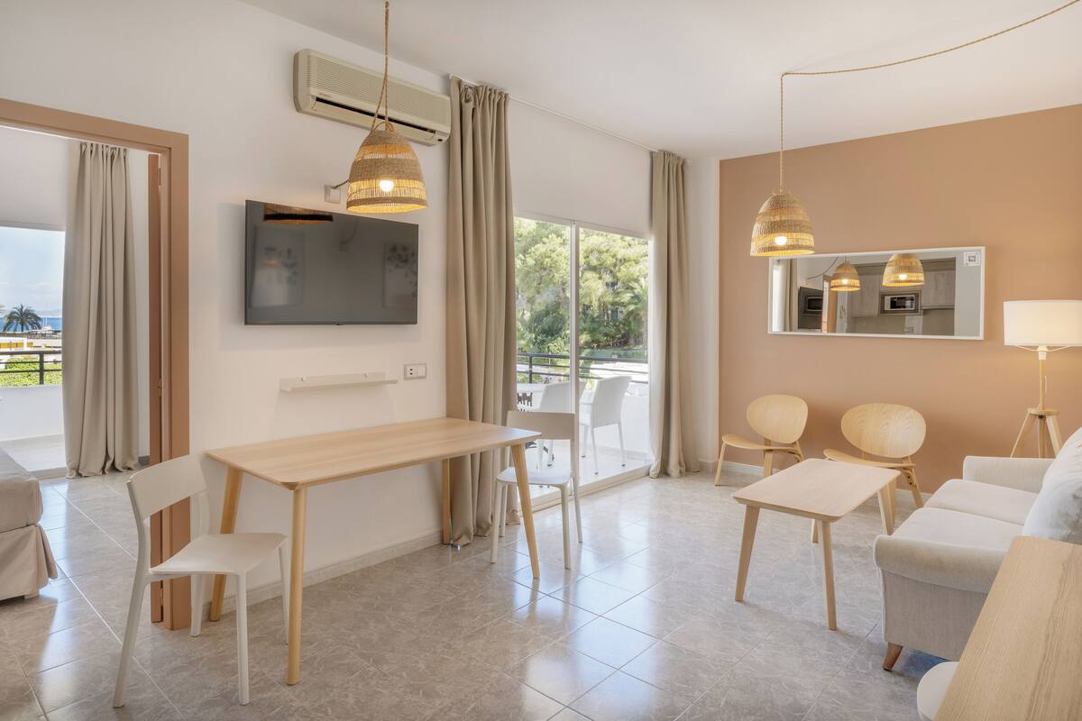 Ein modernes Wohnzimmer mit einem Holztisch, weißen Stühlen, einer Couch und einem an der Wand montierten Fernseher.