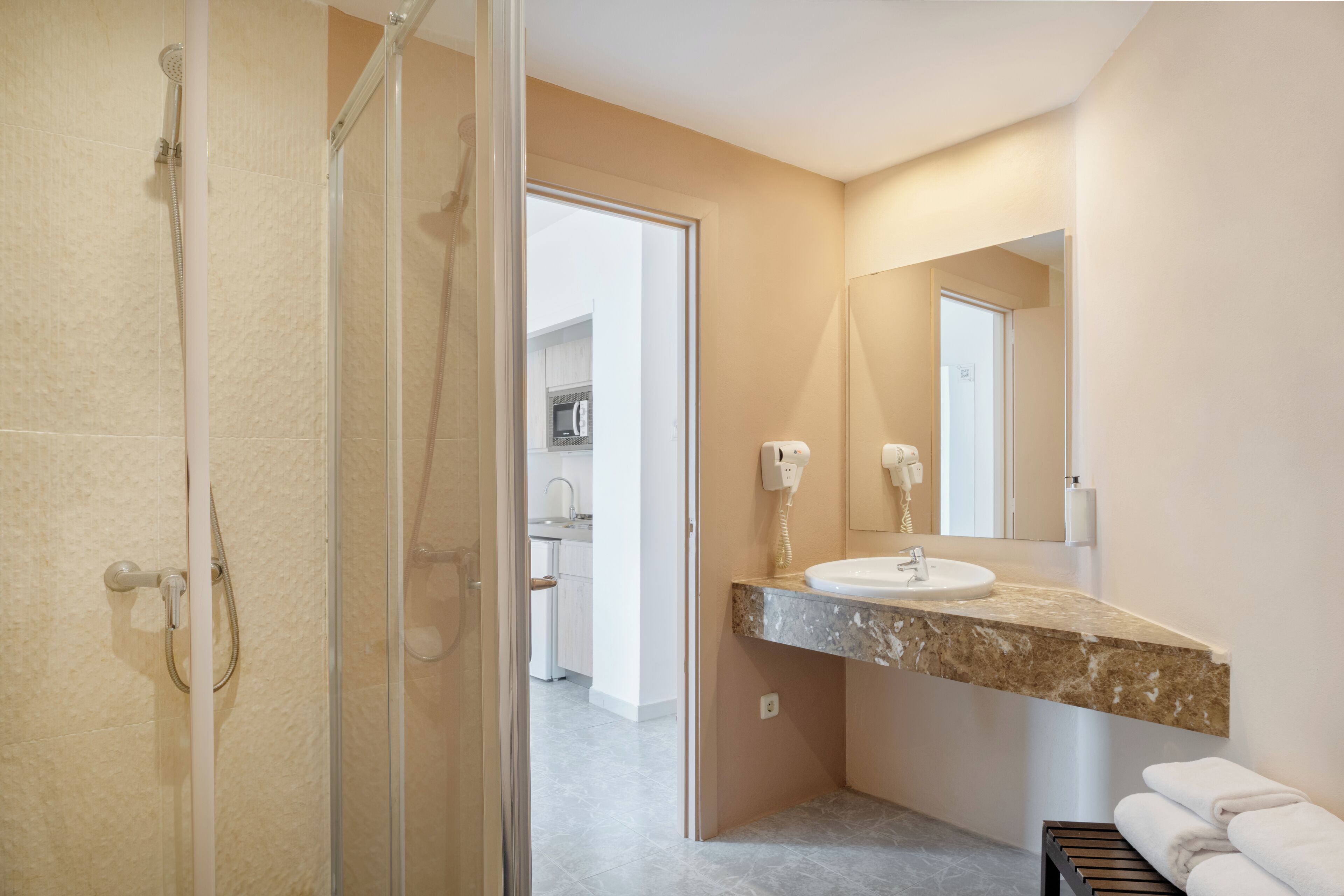 Un baño moderno con cabina de ducha de vidrio, lavamanos de mármol y un toallero visible.