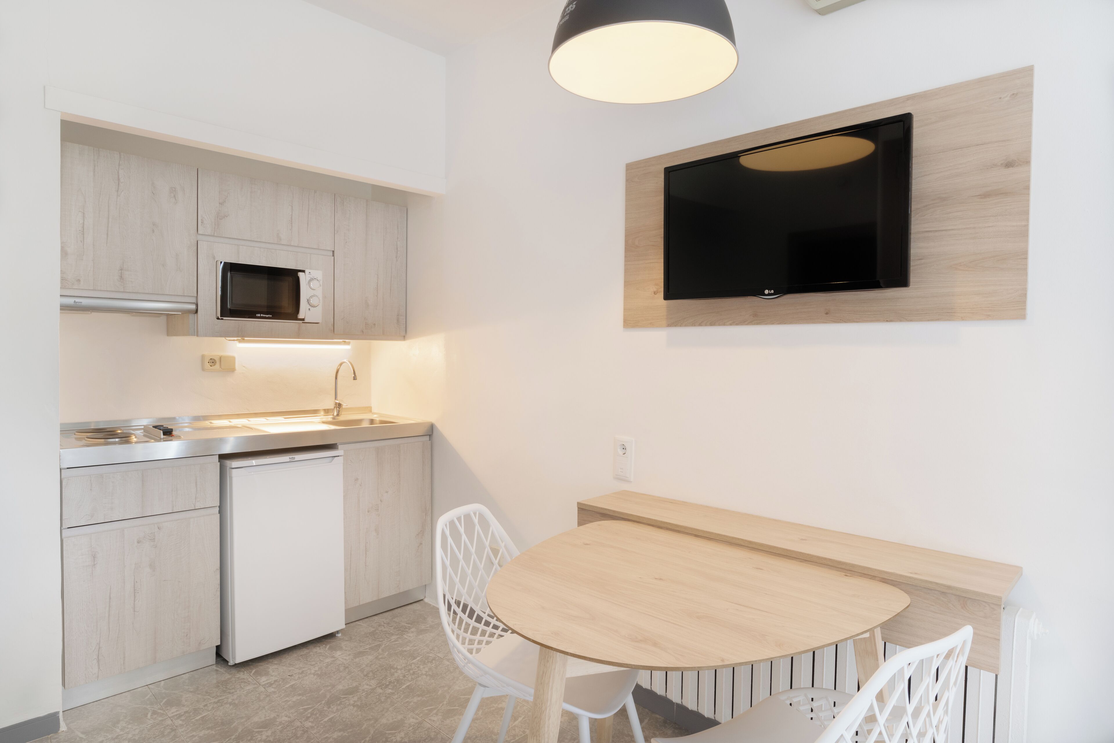 Cozinha moderna com micro-ondas, máquina de lavar louça e uma mesa de jantar de madeira com cadeiras brancas.