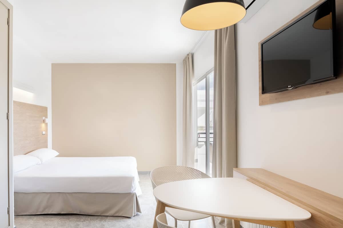 Ein Hotelzimmer mit Bett, Tisch, Stühlen, Fernseher und einem Fenster mit Vorhängen.