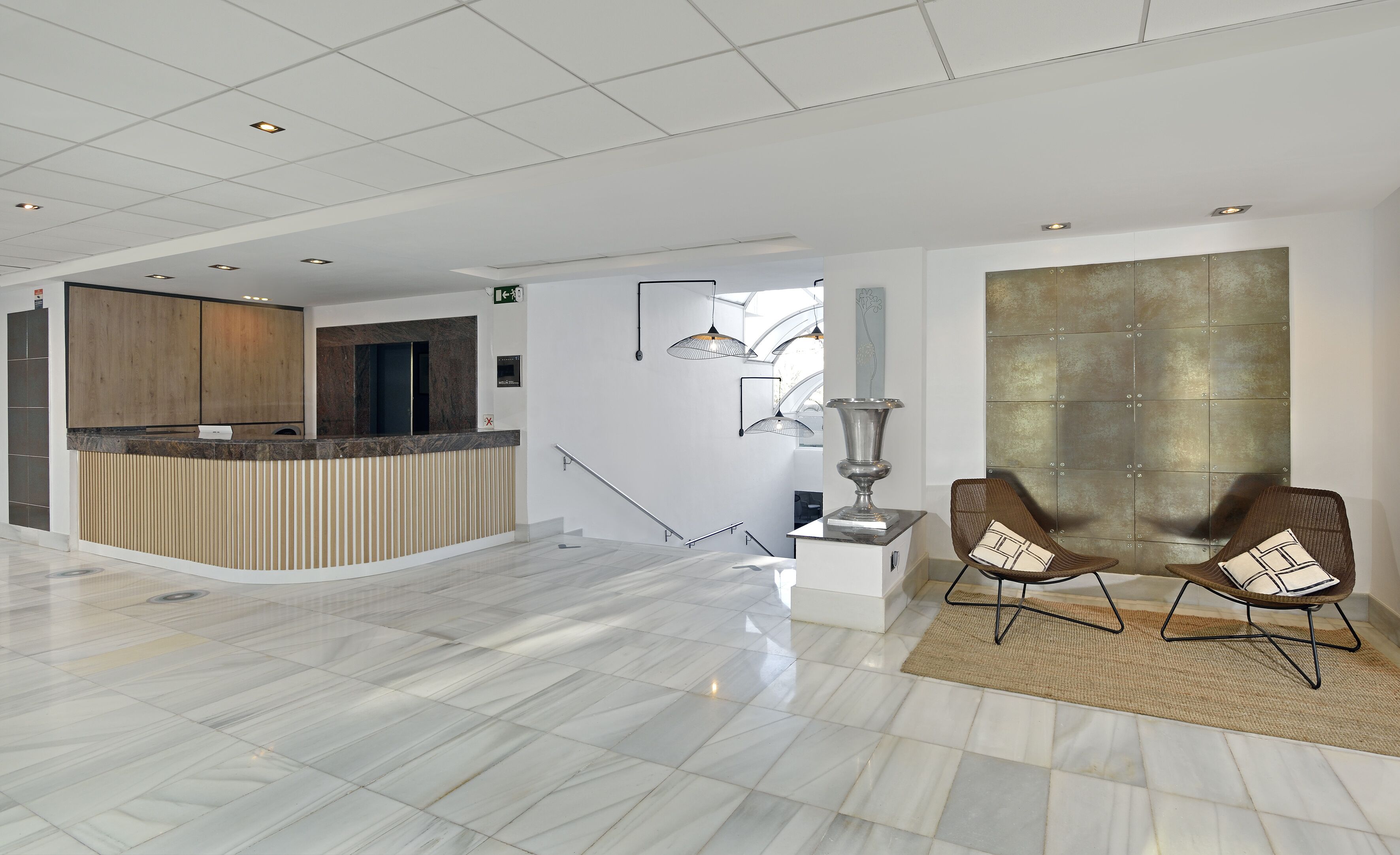 Een moderne lobby met een receptiebalie, een trap en twee zithoeken.