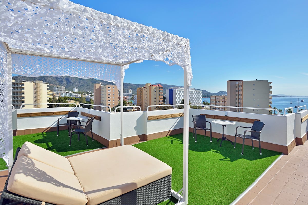 Eine Dachterrasse mit Kunstrasen, Sitzmöglichkeiten im Freien und Blick auf das Meer und die Gebäude.