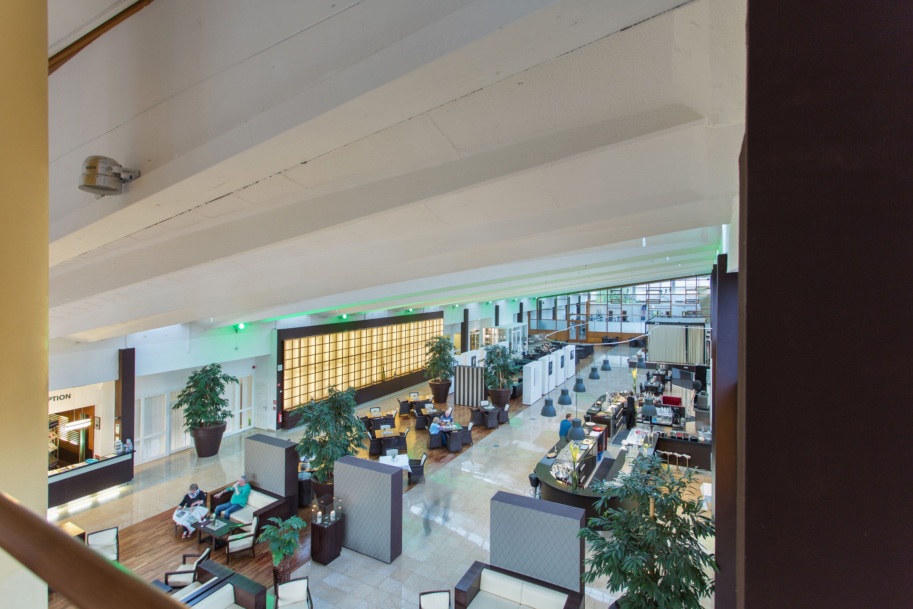 A spacious lobby with seating areas, a reception desk, and large potted plants.