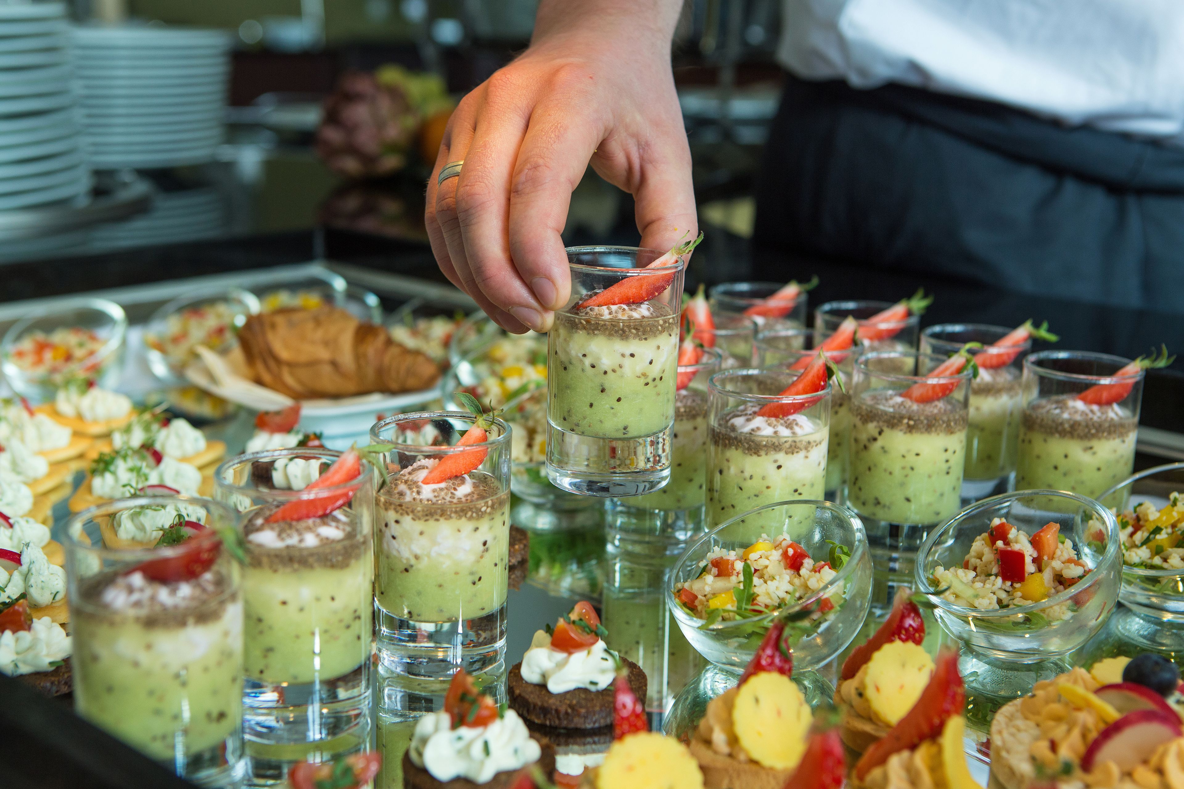 Eine Auswahl an Speisen an einem Buffet, darunter kleine Gläser mit grünem Dessert und verschiedene andere Gerichte.