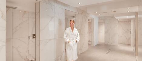 A modern bathroom with marble walls and a glass shower enclosure.