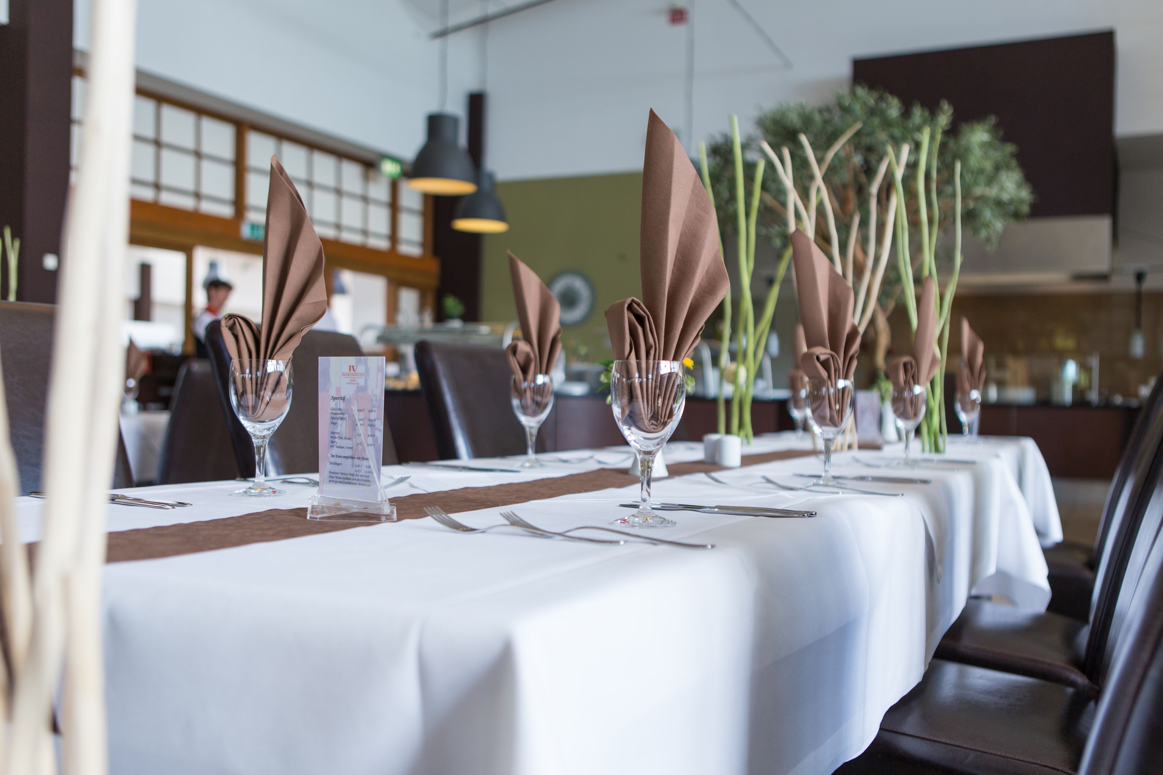 A restaurant with white tablecloths, neatly folded brown napkins, and clear glassware.